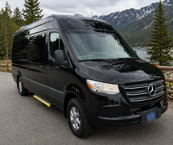 Black Mercedes-Benz Sprinter van parked on a paved road with a mountain and lake in the background.