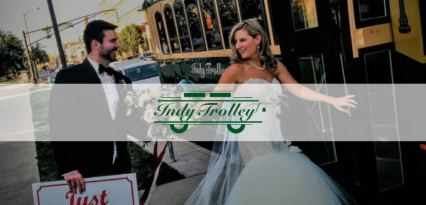 A bride and groom posing next to a vintage-style trolley with 'Indy Trolley' branding.