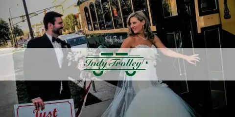 A bride and groom posing next to a vintage-style trolley with 'Indy Trolley' branding.