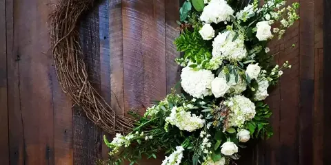 A white floral wedding arrangement with roses and hydrangeas mounted on a dark wooden panel.