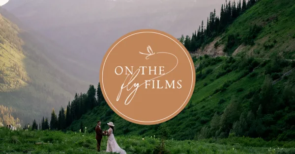 A wedding couple standing in a mountain meadow with a large 'On The Fly Films' logo overlaid in the center.