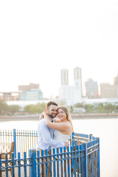 A smiling couple embracing outdoors with a city skyline in the background.