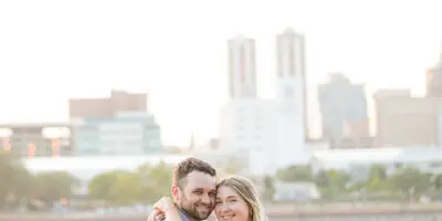 A smiling couple embracing outdoors with a city skyline in the background.