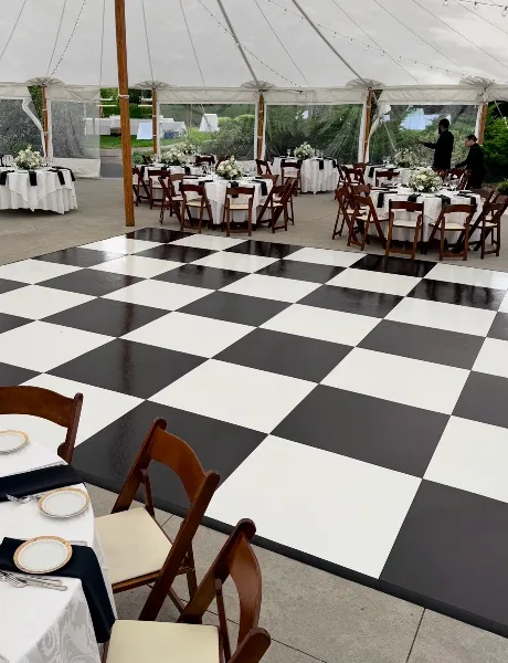 A black and white checkered dance floor installed in a white tent at a wedding reception.