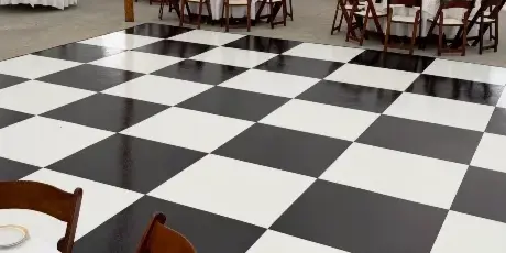 A black and white checkered dance floor installed in a white tent at a wedding reception.