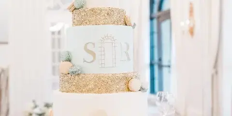 A multi-tiered white and gold wedding cake decorated with macarons and fresh flowers on a gold stand.