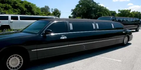 A black stretch limousine parked in a lot with other vehicles in the background.