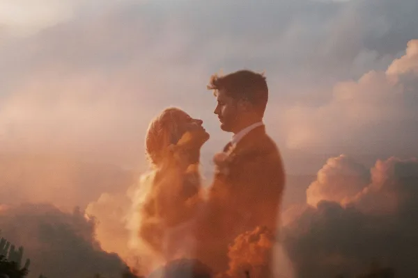 Cinematic double-exposure photograph of a couple in profile against a cloudy sky.