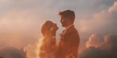 Cinematic double-exposure photograph of a couple in profile against a cloudy sky.