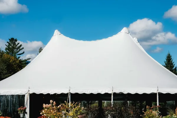 A large white peaked event tent set up outdoors against a blue sky with trees in the background.