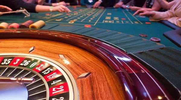 Close-up of a casino roulette wheel and green felt gaming table with chips and players' hands.