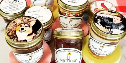 An assortment of Sunflour Baking Company cake jars with custom lids arranged on a red and white checkered tablecloth.