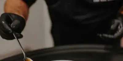 A chef in a black apron with the Thyme to Cater logo is carefully spooning sauce over a plated meal.