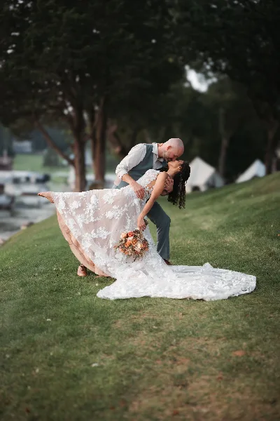 A professional wedding photograph of a bride and groom sharing a kiss in a dip pose on a grassy lawn.