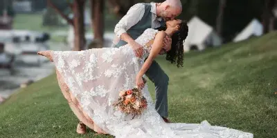 A professional wedding photograph of a bride and groom sharing a kiss in a dip pose on a grassy lawn.