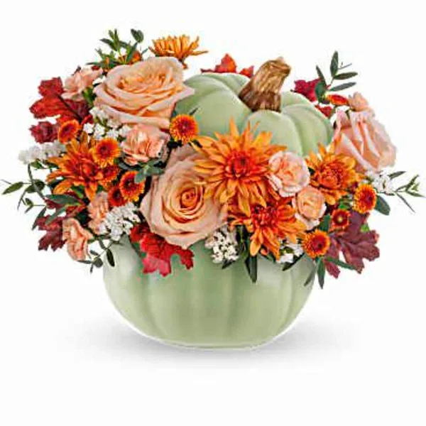 A floral arrangement featuring peach roses, orange daisies, and red maple leaves arranged in a green pumpkin-shaped vase.