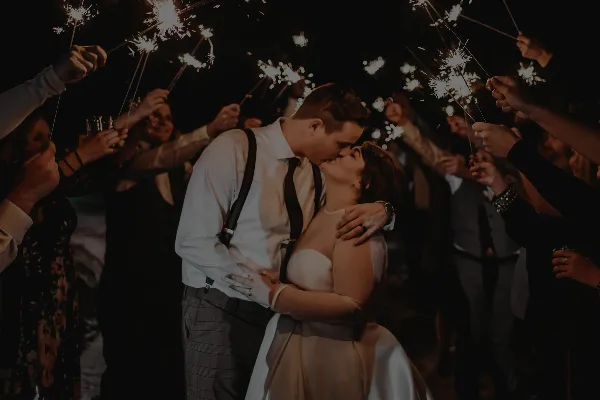 A bride and groom kissing during a sparkler send-off at a wedding reception.