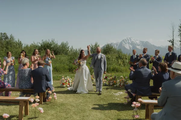 Bride and groom walking down the aisle at an outdoor wedding ceremony with mountains in the background.