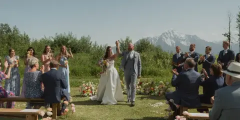 Bride and groom walking down the aisle at an outdoor wedding ceremony with mountains in the background.