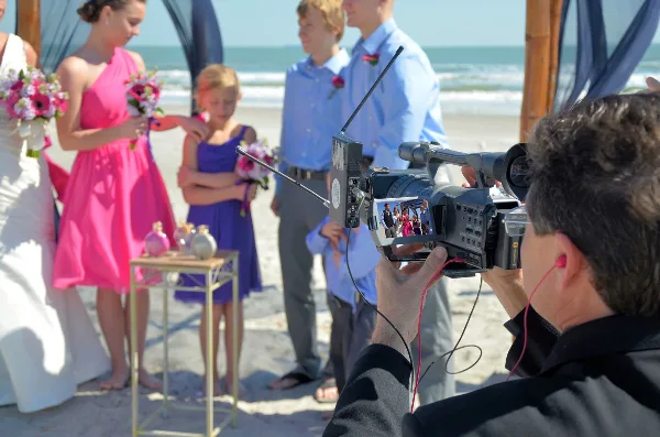 A professional videographer filming a beach wedding ceremony with a high-definition camera.