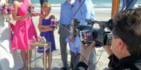 A professional videographer filming a beach wedding ceremony with a high-definition camera.