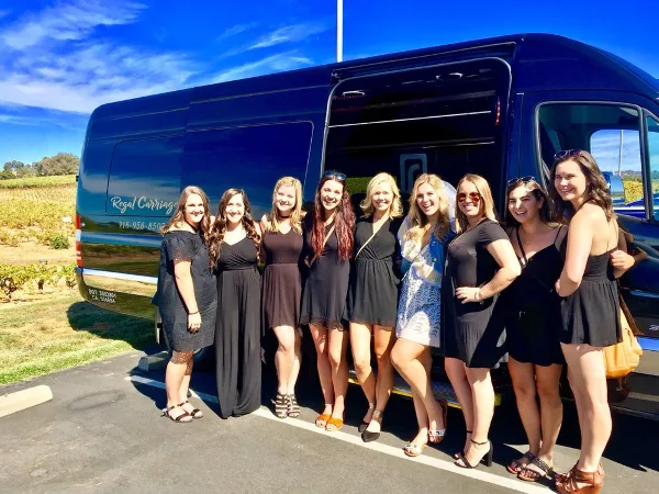 A group of women posing in front of a dark blue party bus with 'Regal Carriage' branding and a phone number on the side.