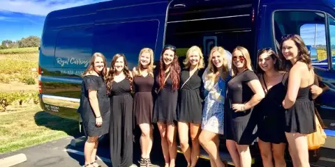 A group of women posing in front of a dark blue party bus with 'Regal Carriage' branding and a phone number on the side.