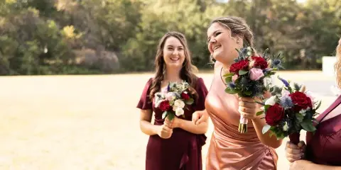 Bridesmaids in maroon dresses holding floral bouquets outdoors