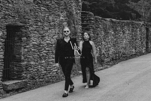 Black and white photo of a couple walking on a path next to a stone wall