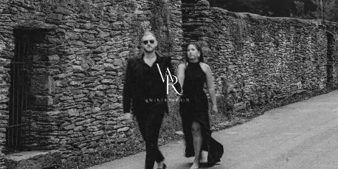 Black and white photo of a couple walking on a path next to a stone wall