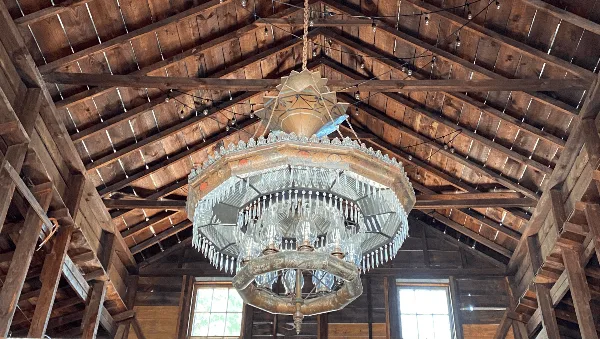 Interior view of a rustic barn event venue featuring a large, ornate chandelier hanging from a high wooden ceiling.