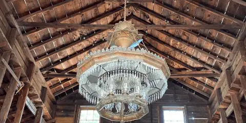 Interior view of a rustic barn event venue featuring a large, ornate chandelier hanging from a high wooden ceiling.