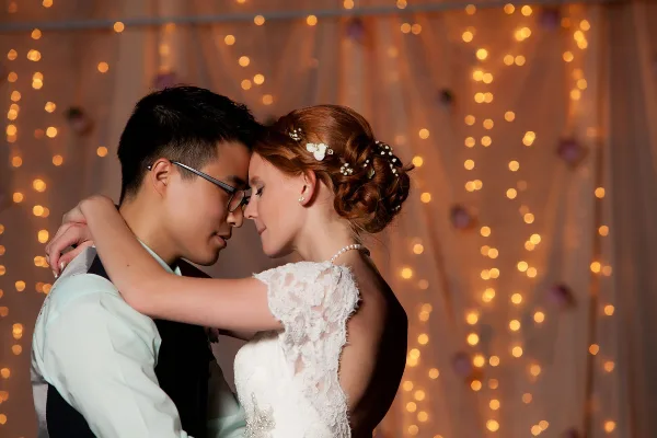 A bride and groom embracing in front of a backdrop of warm string lights.