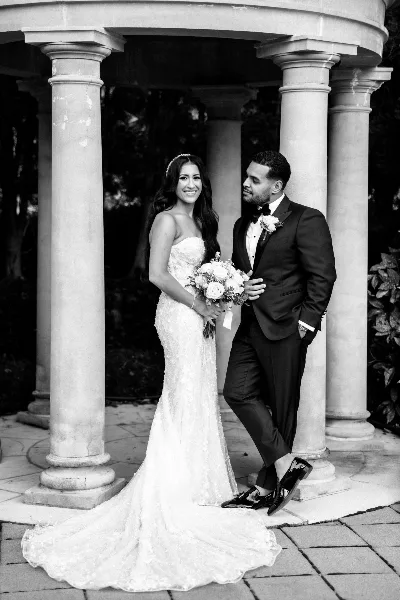 A bride and groom posing in a stone gazebo at a wedding venue.
