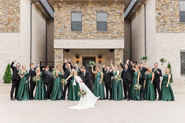 A wedding party posing in front of a stone and brick venue building.