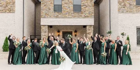 A wedding party posing in front of a stone and brick venue building.
