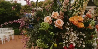 A tall, organic wedding floral arrangement featuring cream roses, foxgloves, and cascading greenery on a white pedestal.