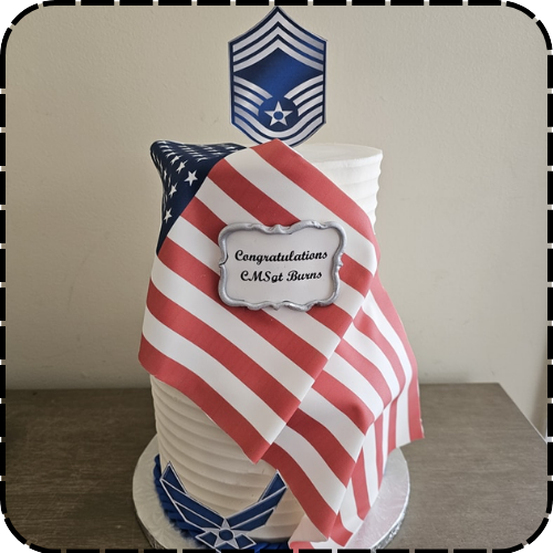 A custom decorated cake featuring a draped American flag and a military rank insignia topper.