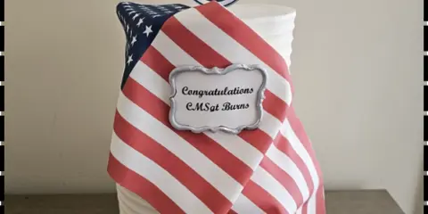 A custom decorated cake featuring a draped American flag and a military rank insignia topper.