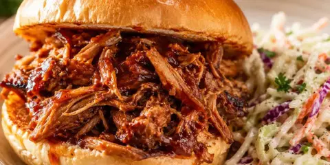 A BBQ pork sandwich served with a side of coleslaw on a plate.