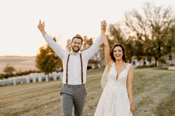 A bride and groom celebrating with arms raised at an outdoor wedding venue.