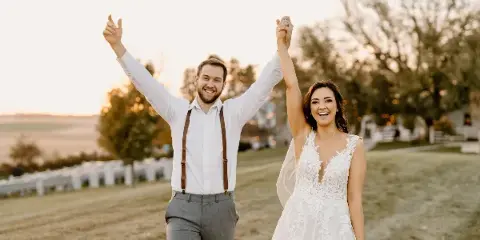 A bride and groom celebrating with arms raised at an outdoor wedding venue.
