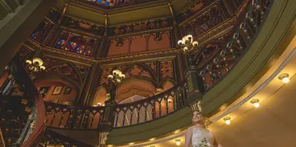 A bride in a white wedding dress stands on a grand staircase with a stained glass ceiling.