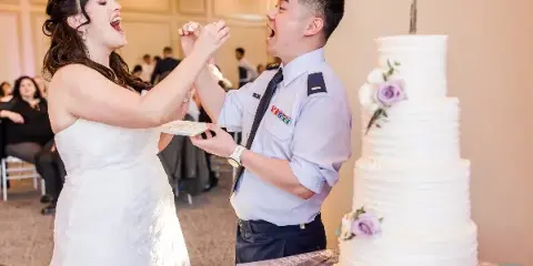 A bride and groom sharing a playful moment with cake at a wedding reception, with a multi-tiered wedding cake in the foreground.