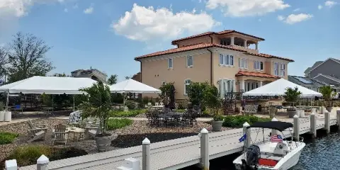 Outdoor event setup with white tents, tables, and chairs near a waterfront venue