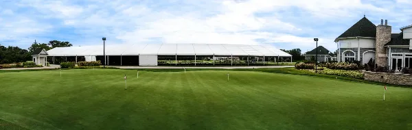 A large white event tent set up on a green lawn next to a stone building.