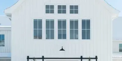 Exterior view of a white modern farmhouse barn with a weathervane and sliding doors in a snowy landscape.