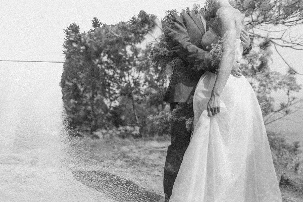 Black and white photograph of a bride and groom embracing outdoors near a body of water.