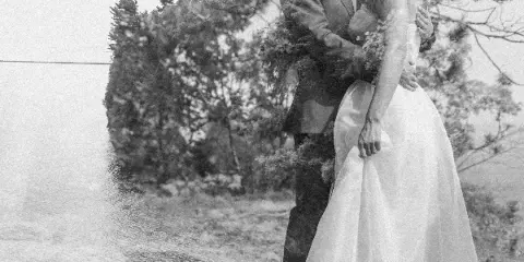 Black and white photograph of a bride and groom embracing outdoors near a body of water.