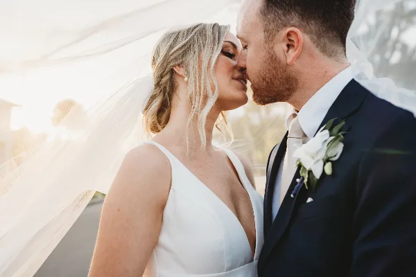 A bride and groom sharing a close moment, with the bride wearing a white dress and veil and the groom in a dark suit with a white boutonniere.